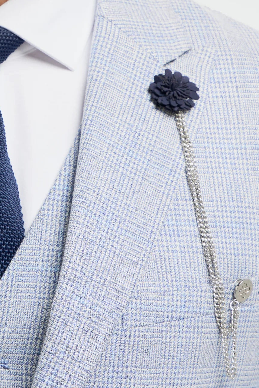 Man wearing a light gray suit with a navy tie and flower pin on a white background