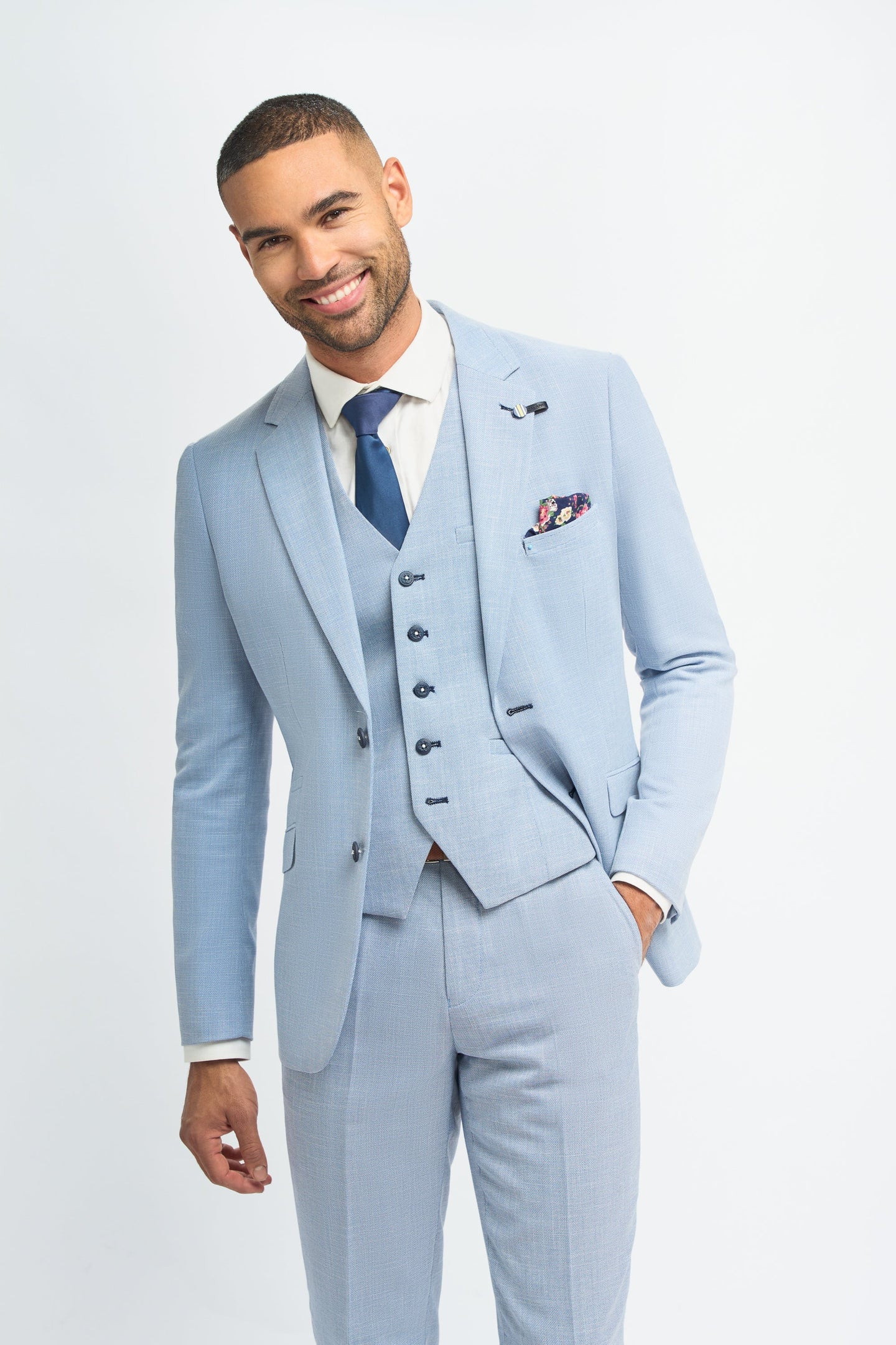 Man wearing a light blue suit with a white shirt and blue tie on a plain background